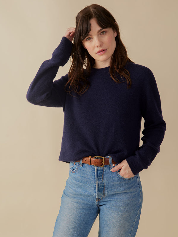 Woman wearing a navy cashmere sweater and blue jeans against a beige background