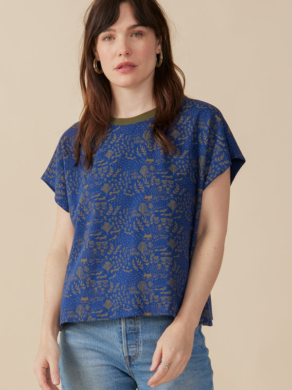 Woman wearing a blue patterned top with Fox print and jeans on a beige background