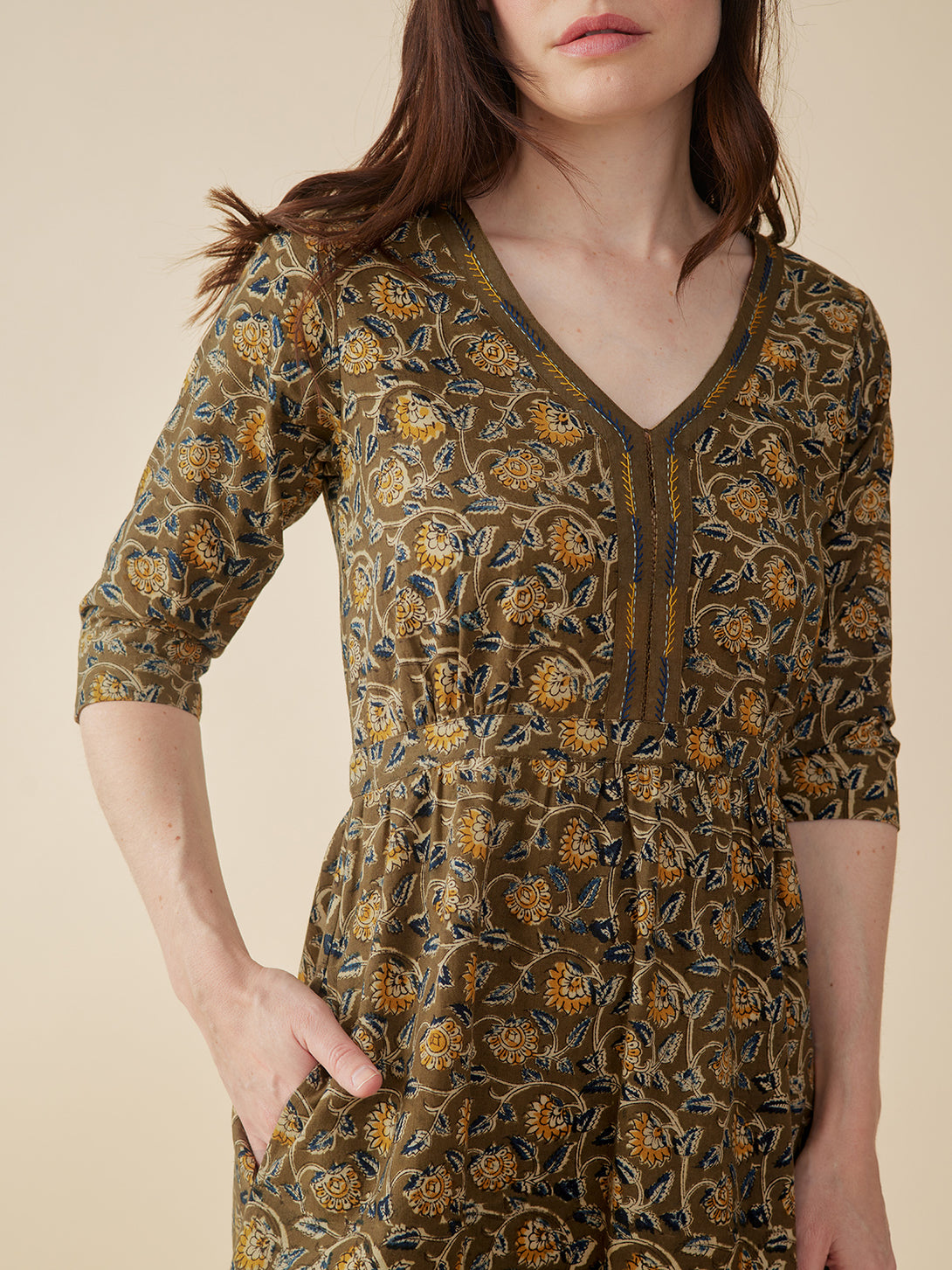 Woman wearing a patterned dress with  pockets on a neutral background 