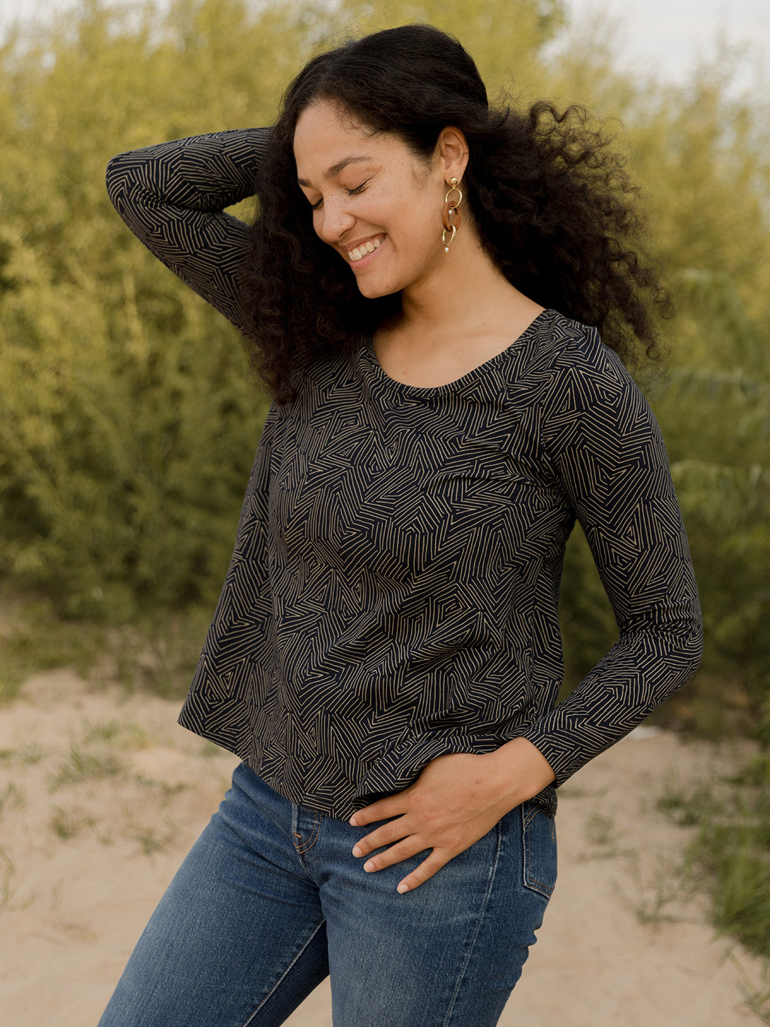 Woman wearing a black patterned long-sleeve top and blue jeans outdoors.