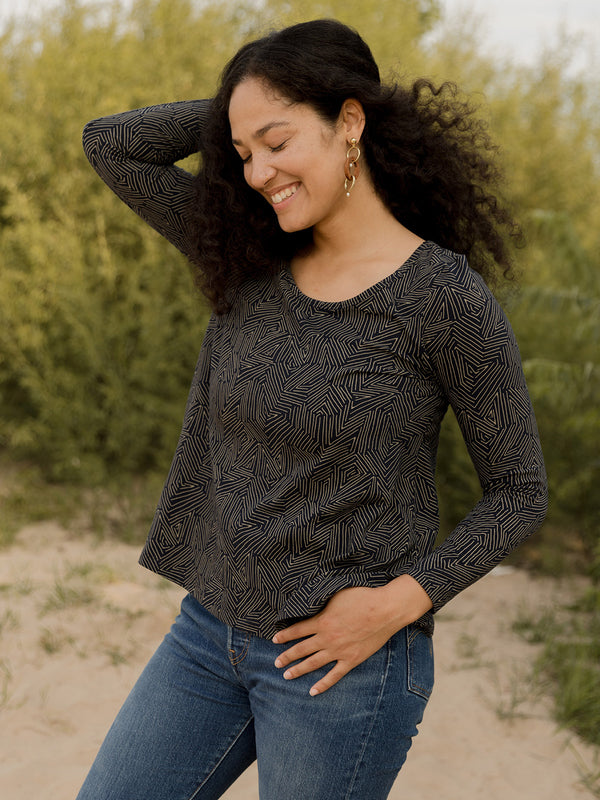 Woman wearing a black patterned long-sleeve top and blue jeans outdoors.